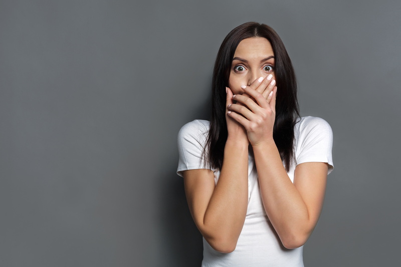 woman-looking-shocked-and-covering-mouth-on-grey-background