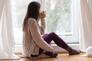 person-looking-out-window-and-drinking-from-mug